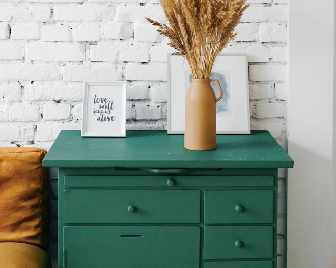 A green dresser with a vase and framed quotes on top of it